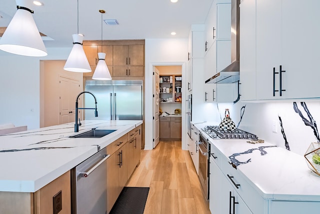 kitchen with a center island with sink, wall chimney range hood, white cabinetry, and pendant lighting