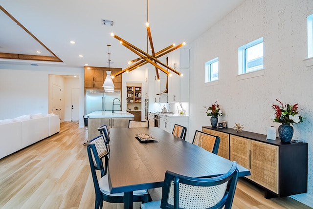 dining room with sink, a tray ceiling, a chandelier, and light hardwood / wood-style floors