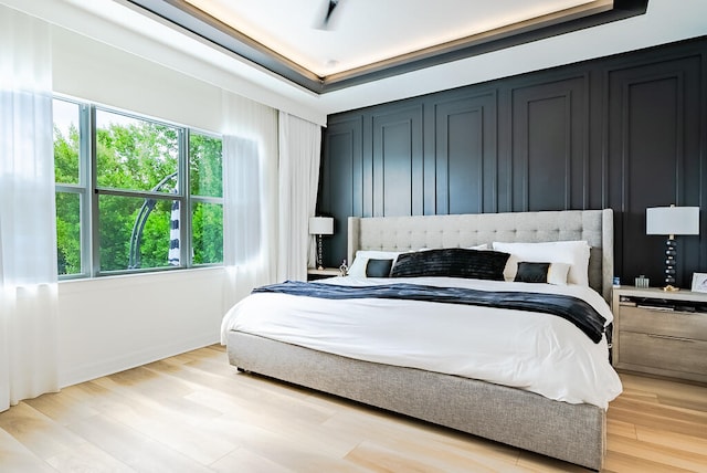 bedroom with light wood-type flooring and a tray ceiling