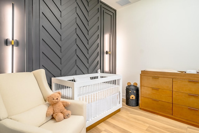 bedroom with light wood-type flooring and a nursery area