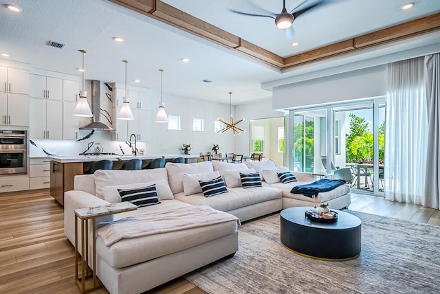 living room with light hardwood / wood-style flooring, ceiling fan with notable chandelier, and sink