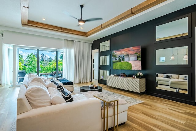 living room featuring light hardwood / wood-style flooring, a tray ceiling, and ceiling fan