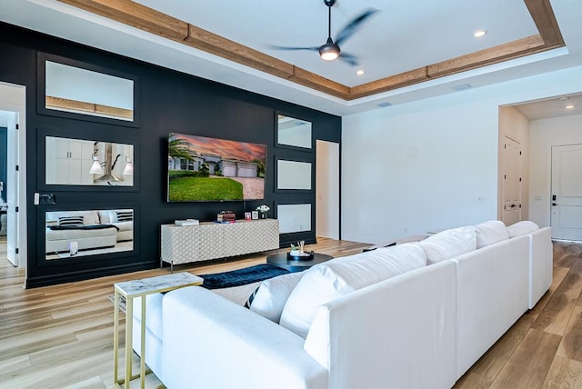 living room with a raised ceiling, light hardwood / wood-style floors, and ceiling fan