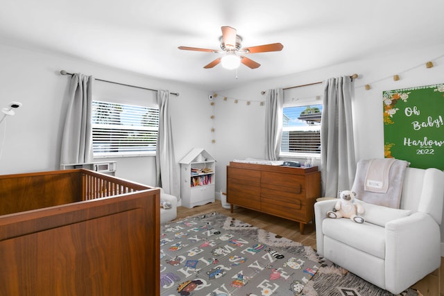 bedroom featuring multiple windows, ceiling fan, a nursery area, and hardwood / wood-style flooring