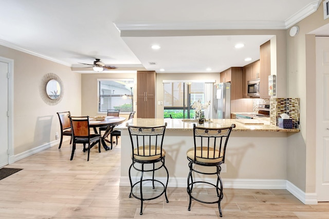 kitchen featuring appliances with stainless steel finishes, kitchen peninsula, backsplash, and light hardwood / wood-style floors