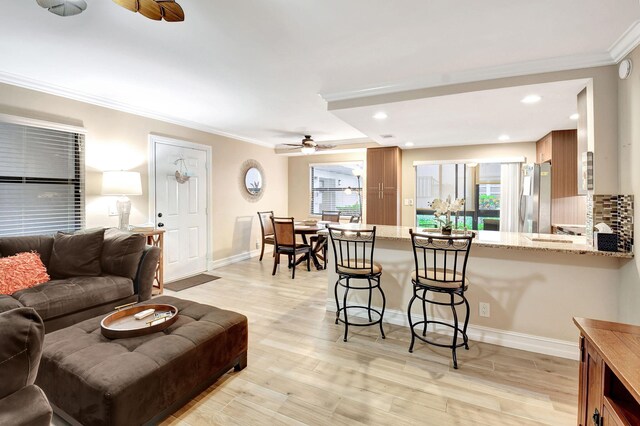 living room with light wood-type flooring, ornamental molding, and ceiling fan