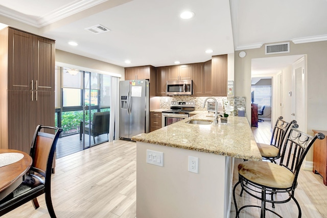 kitchen featuring backsplash, light wood-type flooring, light stone countertops, stainless steel appliances, and sink