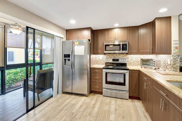 kitchen featuring light wood-type flooring, a wealth of natural light, stainless steel appliances, and light stone countertops