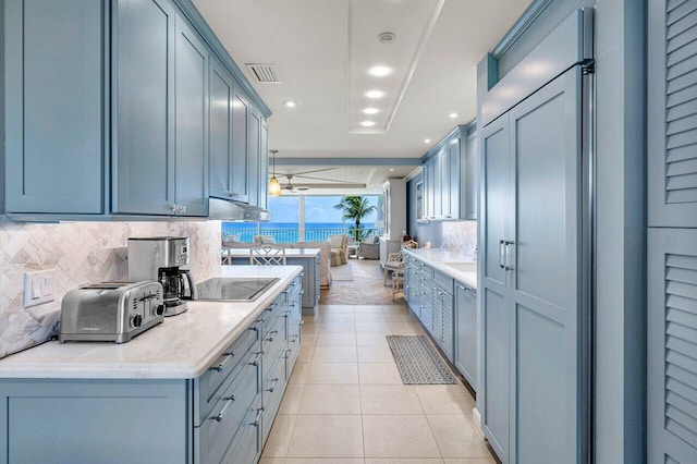 kitchen with light tile patterned floors, tasteful backsplash, ceiling fan, black electric cooktop, and a water view