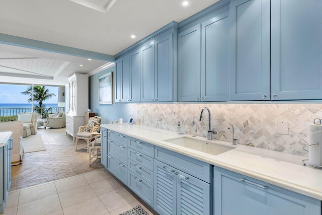 kitchen featuring a water view, backsplash, light tile patterned floors, sink, and blue cabinets