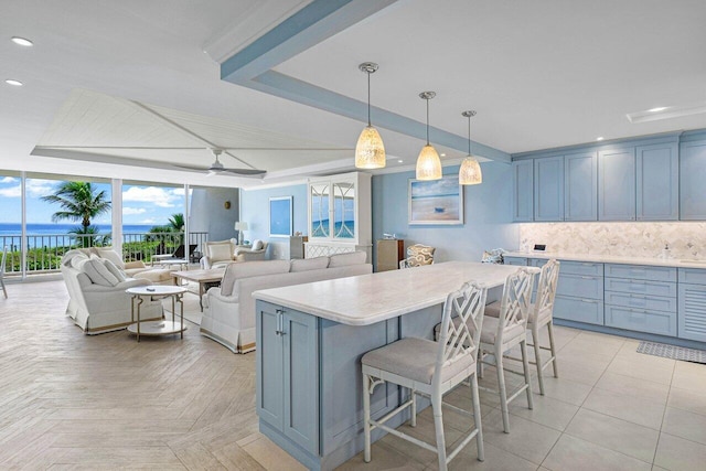 kitchen with backsplash, ceiling fan, hanging light fixtures, a tray ceiling, and a breakfast bar