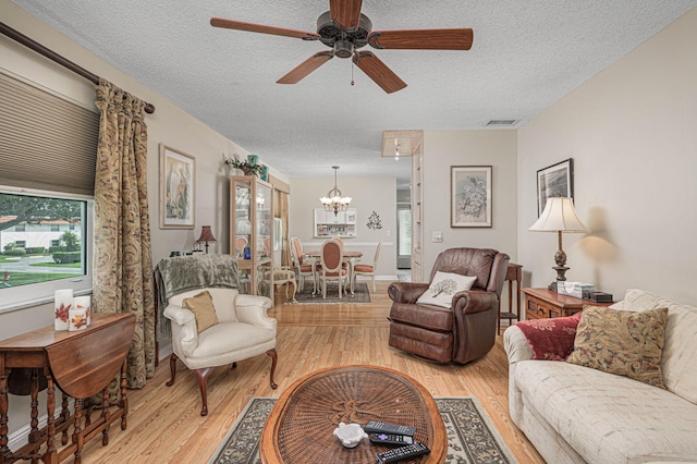 living room with ceiling fan with notable chandelier, light wood-type flooring, a textured ceiling, and a healthy amount of sunlight