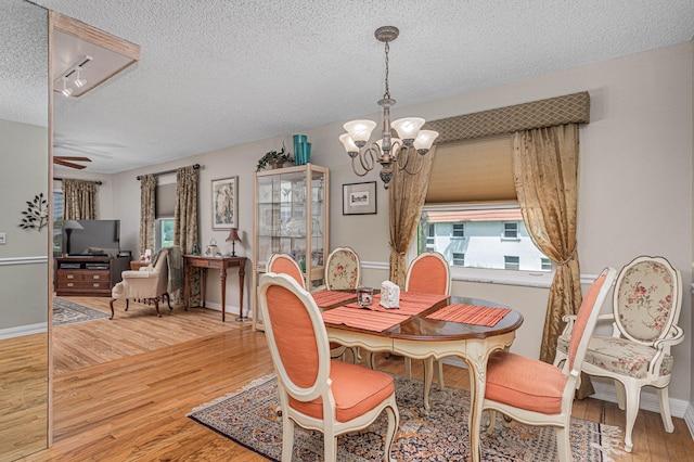 dining area with a textured ceiling, light hardwood / wood-style flooring, and ceiling fan with notable chandelier