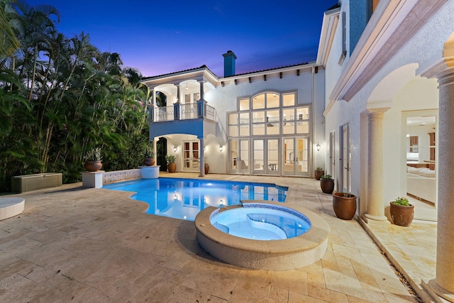 pool at dusk featuring a patio area and an in ground hot tub