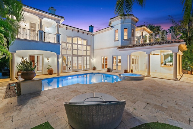 13058 Flamingo Ter, Palm Beach Gardens, FL 33410 - back of property at dusk featuring french doors, a balcony, a patio area, a pool with connected hot tub, and stucco siding