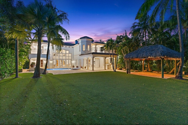 back house at dusk featuring a balcony, a gazebo, a yard, and a patio area