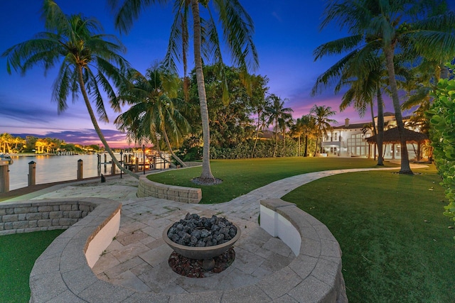 yard at dusk featuring a water view, a patio, and a fire pit