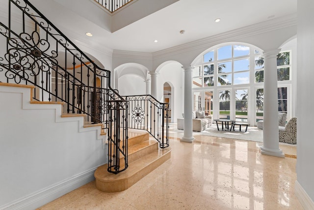 entryway with crown molding, a towering ceiling, and decorative columns