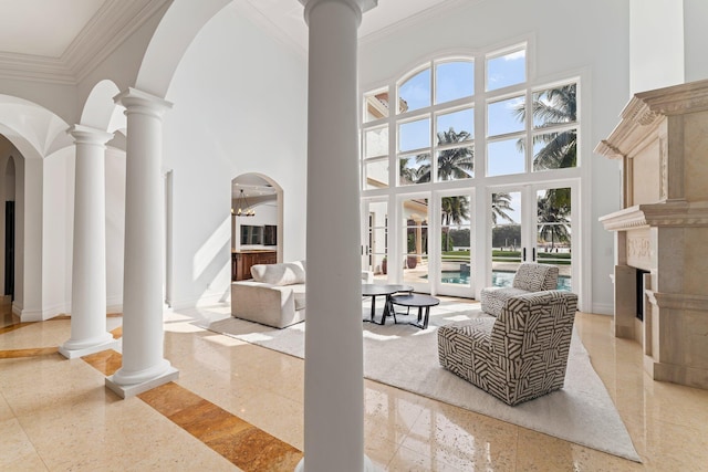 living room featuring a fireplace, french doors, ornate columns, ornamental molding, and a high ceiling