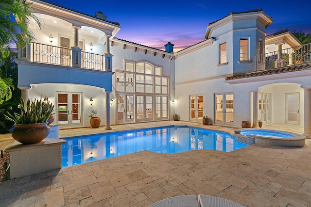 pool at dusk with an in ground hot tub, french doors, and a patio