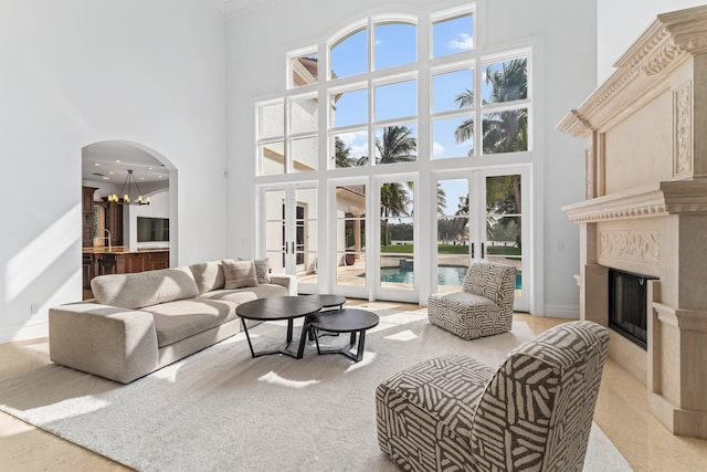 living room featuring an inviting chandelier, crown molding, a high end fireplace, french doors, and a high ceiling