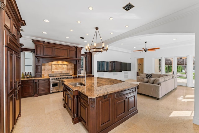 kitchen with a kitchen island with sink, high end stainless steel range oven, ceiling fan with notable chandelier, ornamental molding, and sink