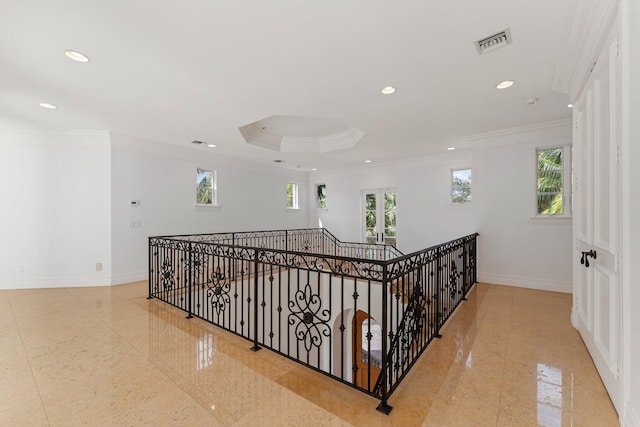 hall with a raised ceiling and ornamental molding