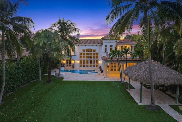 13058 Flamingo Ter, Palm Beach Gardens, FL 33410 - back of property at dusk with french doors, a patio, a lawn, a tile roof, and an outdoor pool