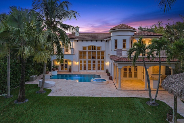 13058 Flamingo Ter, Palm Beach Gardens, FL 33410 - back of property at dusk with a balcony, french doors, a patio, and a lawn
