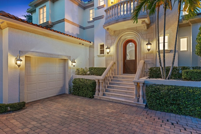 exterior entry at dusk featuring a balcony and a garage