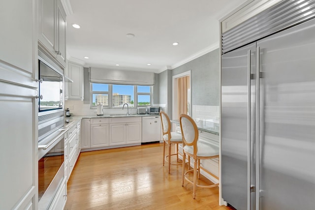 kitchen with crown molding, decorative backsplash, light wood-type flooring, white cabinetry, and stainless steel appliances