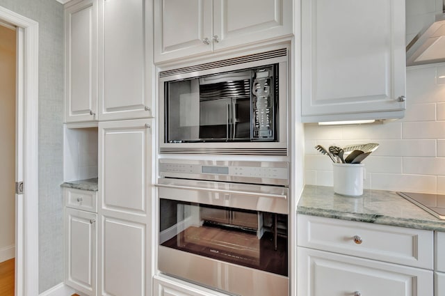 kitchen with tasteful backsplash, light stone countertops, range hood, appliances with stainless steel finishes, and white cabinetry