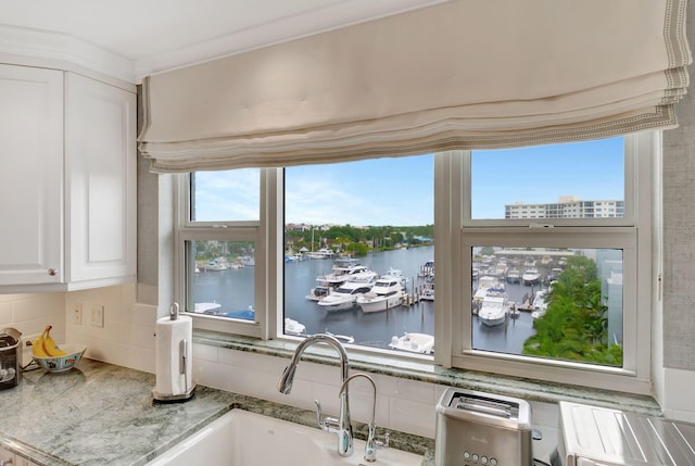 interior space featuring white cabinetry, sink, light stone countertops, tasteful backsplash, and a water view