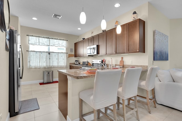 kitchen with decorative light fixtures, stainless steel appliances, kitchen peninsula, a breakfast bar, and light tile patterned flooring