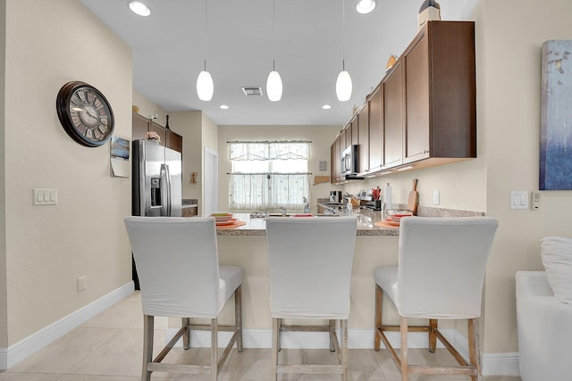 kitchen featuring a breakfast bar area, pendant lighting, appliances with stainless steel finishes, kitchen peninsula, and light tile patterned flooring