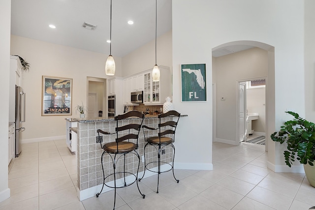 kitchen featuring appliances with stainless steel finishes, pendant lighting, white cabinets, a high ceiling, and light stone countertops