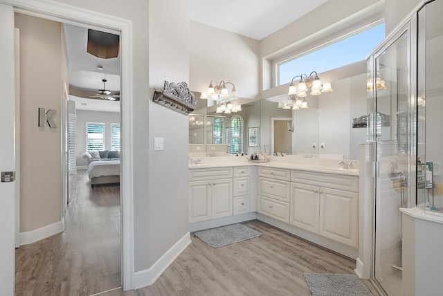 bathroom with ceiling fan with notable chandelier, wood-type flooring, a shower with door, and vanity