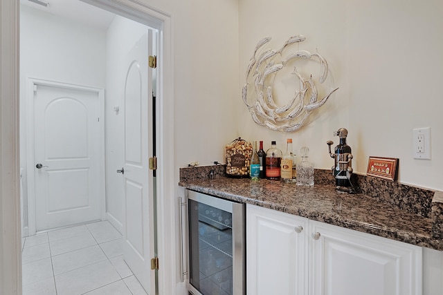 bar featuring white cabinets, light tile patterned floors, beverage cooler, and dark stone counters