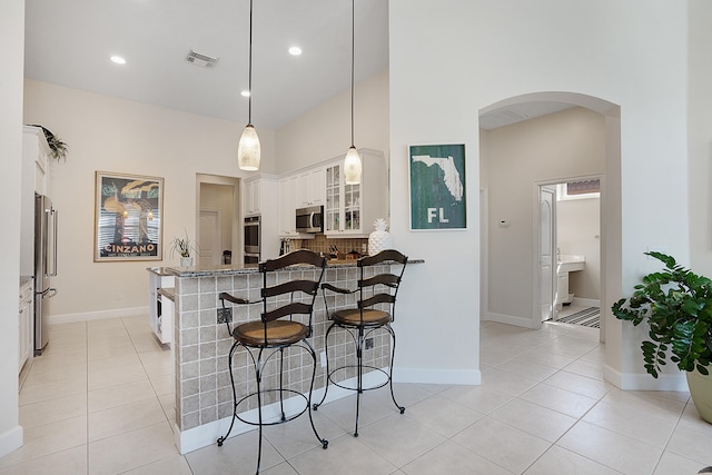 kitchen featuring white cabinets, appliances with stainless steel finishes, hanging light fixtures, and light tile patterned flooring