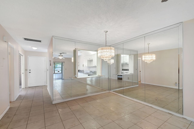 tiled spare room featuring ceiling fan with notable chandelier and a textured ceiling