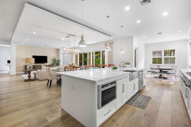 kitchen featuring hanging light fixtures, sink, a kitchen island with sink, white cabinetry, and light hardwood / wood-style floors