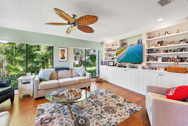 living room with built in shelves, ceiling fan, light hardwood / wood-style floors, and a textured ceiling