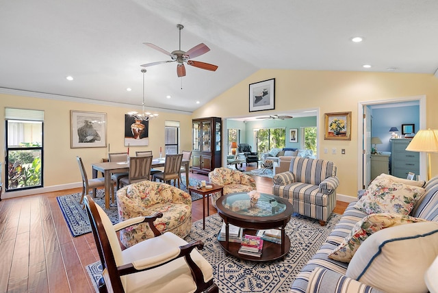 living room with ceiling fan with notable chandelier, hardwood / wood-style flooring, vaulted ceiling, and crown molding