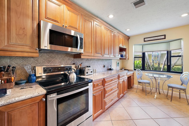 kitchen with light stone countertops, appliances with stainless steel finishes, decorative backsplash, and light tile patterned floors