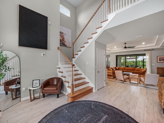 staircase featuring a raised ceiling, ceiling fan, a towering ceiling, and hardwood / wood-style flooring