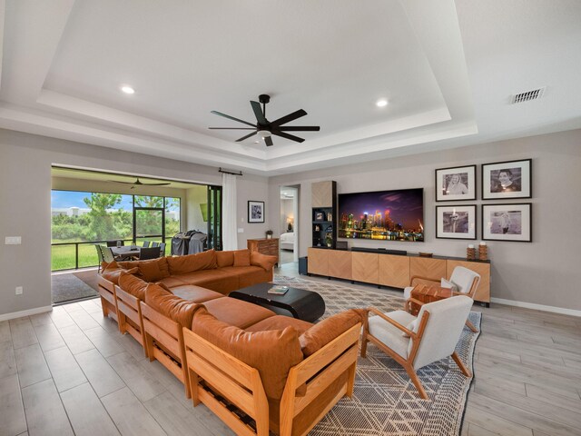 living room featuring a raised ceiling, light hardwood / wood-style flooring, and ceiling fan