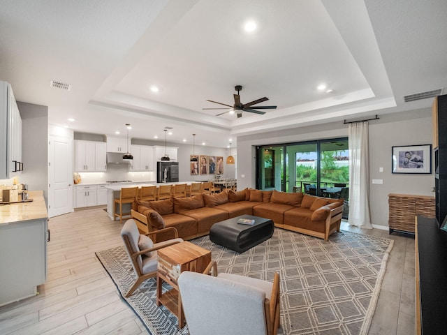 living room featuring a tray ceiling, light wood-type flooring, and ceiling fan