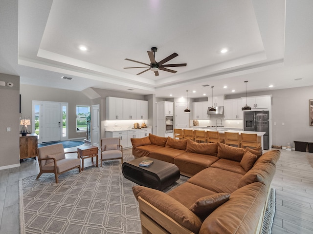 living room with light wood-type flooring, a tray ceiling, and ceiling fan