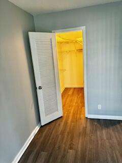 unfurnished bedroom featuring a walk in closet, wood finished floors, and baseboards