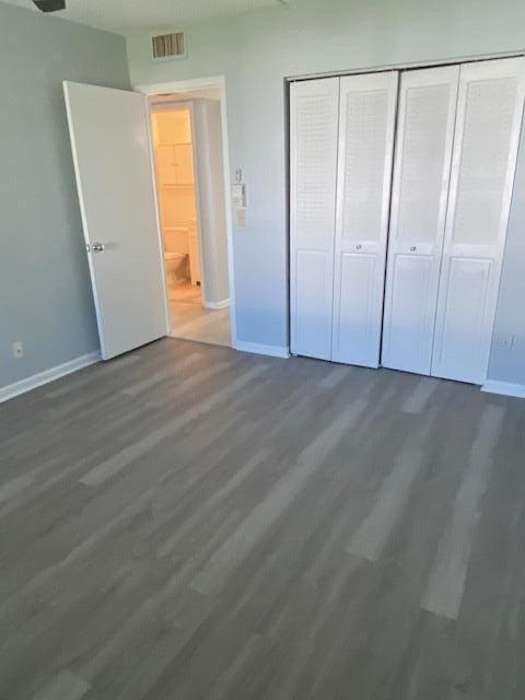 unfurnished bedroom with wood finished floors, visible vents, a closet, and baseboards